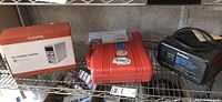 Photo showing boxed Eventek DC Power Supply, orange Volvo tool kit case, and black DieHard battery charger on a metal shelf.