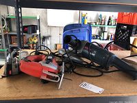 Photo showing three power tools on a workbench: a red and black Black & Decker jig saw, a blue and black Bosch sander, and a Porter-Cable sander in the background. The tools have power cords arranged loosely around them.