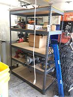 Photo showing four-tier metal shelving with particle board shelves holding some miscellaneous small items, with gray metal frame and light brown wooden shelves.