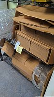 Stacked multiple sizes of flat-packed cardboard boxes on metal shelving, bubble wrap visible in background