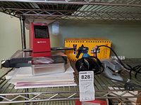 Wolverine film scanner on shelf, showing red scanner, black strip to hold slides. Various papers underneath and a metal case.