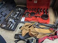 Photo showing 9-way slide hammer puller set in black case, red case with adapters, used leather carpenter belt, and harness straps.