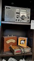 Panasonic 8 Band RF-2200 shortwave radio, Weston AC ammeter in wooden case, and a vintage alarm clock radio on shelf.