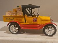 Side view of diecast model truck showing yellow and red paint, black top, chrome wheels, and Arm & Hammer product boxes in the truck bed