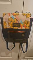 Full view of the mini backpack hanging on a white door, showing multicolor pattern on top and solid navy bottom.
