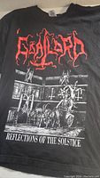 Front of black T-shirt showing red Goatlord logo above detailed black and white graphic with figures and text 'Reflections of the Solstice'