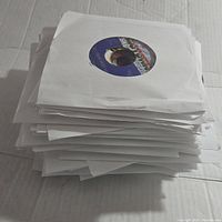 Stack of assorted vintage 45 RPM vinyl records in white paper sleeves.