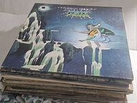 Stack of vintage rock vinyl LPs with an illustrated fantasy/sci-fi album cover on top.