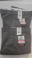 Two pairs of folded charcoal gray Dickies 874 work pants showing front and waistband with tags.