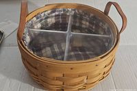 Woven Longaberger basket with two handles, clear plastic insert divided into four compartments visible, fabric liner with plaid pattern.