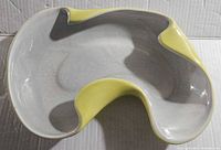 Top and angled view showing kidney shape and yellow accent glazes inlaid on a smooth gray ceramic.