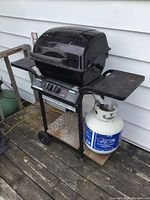 Full view of black Master Chef propane BBQ with side shelves, propane tank attached, and mounted on a wheeled cart.