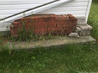 Wide view of the stacked red bricks and the grey paver stones beside them, showing quantity and condition outdoors.