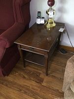 Wooden end table next to a red chair with a lamp and cordless phone on top, showing tabletop surface and legs