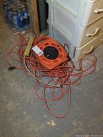 Orange extension cord on black and orange reel with multiple outlets, tangled cord visible