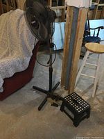 Pedestal fan with distorted front dome along with Eco Fan and folding step stool in basement setting.