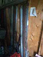 Two 5 feet long metal loading ramps leaning against wooden wall, showing perforated surface and rust