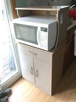 Front view of the microwave stand with a microwave on top, showing the drawer and cabinet doors below.