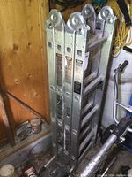 Photo of folded aluminum multi-use ladder from the side, showing flat rungs and hinge points.