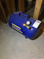 Side view of blue 5 gallon portable air tank showing handle, pressure gauge, outlet valve and label.
