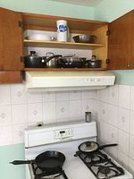 Wide view of kitchen cupboard with pots and pans and bowls on shelves and cast iron pan on stove burner