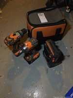 Soft carrying case at rear with two cordless tools and radio on floor