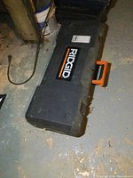 Closed black plastic carrying case with Ridgid logo on top and orange handle