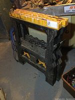 Pair of plastic folding sawhorses with yellow tops and black legs showing wear