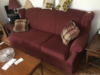 Full front view of the burgundy 3-seat sofa with four cushions placed on the seat and backrest, wooden floor, and adjacent side tables visible.