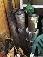 Five used stove pipes leaning against a wall and stacked, showing condition and size.