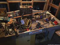 Workbench surface cluttered with various hand tools, wire, and storage drawers.