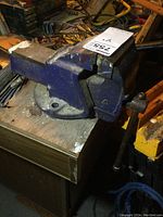 Side view of the blue bench vise mounted on a wooden surface, showing wear and rust.