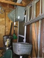 Photo showing two square galvanized metal washtubs hung on wall and the rectangular washtub on the floor with visible aged wear.