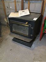 Full view of the SBI black wood stove with glass front door and brass handles along with the manual placed on top.