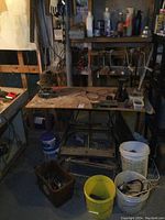 Full view of Black & Decker Workmate 300 workbench showing tabletop with various hand tools, power cords, and hardware scattered on surface. Buckets containing tools are visible below bench.