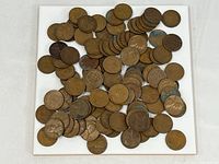 Top view of a large number of Lincoln Wheat pennies spread out on a white surface, showing various tones and conditions.