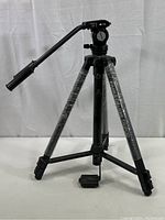 Full view of the black Parks Deluxe video style tripod with double handle and three extendable legs wrapped in protective plastic.