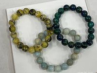 Three quartzite bracelets of different colors laid on a white surface, showing the beads and elastic cord.