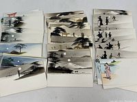 Multiple stacks of vintage Japanese calling cards with hand painted scenes, including Mt. Fuji, people, and landscapes arranged on table.