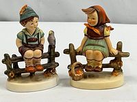Two vintage figurines of children sitting on wooden fences, showing front view and details of both pieces.