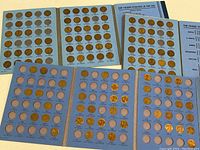 Three blue coin holder books with slots for Lincoln Wheat pennies and later Lincoln Memorial pennies. Books partially filled with copper pennies from 1909 through 1974.