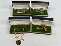Four vintage men's tie clips displayed in original Marbert presentation boxes. Two gold-toned clips and two silver-toned clips, each with a double chain and a round medallion plate for monogramming.