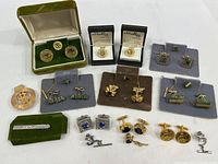 Full view of the collection showing various cufflinks, tie tacks, lapel pins, and a money clip laid out on a flat surface, some in display boxes.