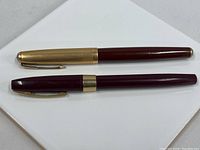 Two vintage fountain pens: one Parker Lifetime with gold-tone cap and burgundy barrel, one burgundy Shaffer pen with silver-tone band.
