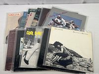 Photo showing a stack of 13 vintage vinyl albums from various artists in archival sleeves with visible album covers including Johnny Guitar Watson, Gino Vannelli, and others.