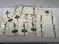 Full lot layout of 14 total items including twin sheets and pillowcases in off-white, all sealed individually in plastic packaging with green ribbons and labels.