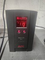 Front view of APC UPS powered on, displaying voltage on red digital screen with two control buttons below