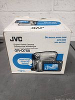 Original box of JVC GR-D750 digital video camera showing 34x optical hyper zoom, auto mode, data battery, and 2.7 inch LCD screen.
