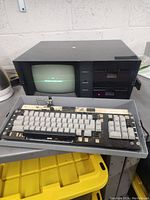 Full view of Kaypro 4 computer with keyboard detached and resting in front. The computer has a CRT monitor and two 5.25-inch floppy drives on the right side.