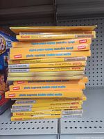Stack of unopened Kodak and Staples photo paper packages arranged vertically on a shelf, showing brand and type labels.